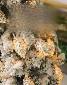 Detailed macro view of pine cone LED string lights with warm glow on snow-covered Christmas tree
