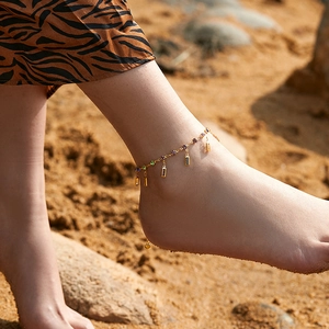 Vintage gold anklet with colorful crystal pendants worn on a beach background