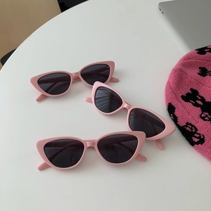 Detailed view of three pairs of retro cat-eye sunglasses with pink frames on white table