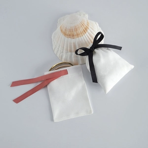 Macro view of white cotton drawstring jewelry pouches with silk ribbon and gold bracelet