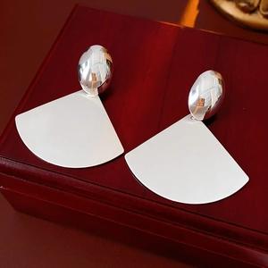 Detail of silver brushed fan earrings on a wooden box showing sleek geometric texture