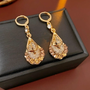 Detailed close-up of golden teardrop earrings with amber and clear zircons on black box