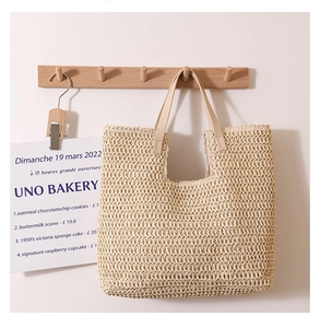 Detail of hand-woven straw tote bag with cream leather handles on a wall hook