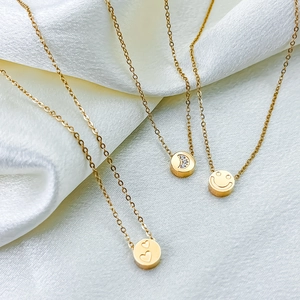 Collana dorata con ciondoli a cuore, luna e faccina su sfondo di seta bianca