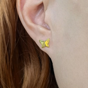 Macro close-up of a gold butterfly stud earring worn on ear showing fine polished details