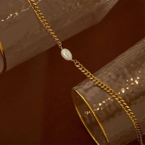 Bohemian 18K gold chain necklace with a white oval pearl draped over textured glassware