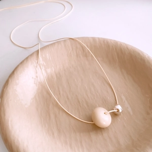 Detail of a minimalist wax rope necklace featuring a large cream ceramic bead and silver accent