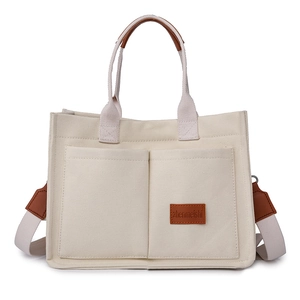 Beige canvas tote bag with brown leather handles and adjustable straps on white background