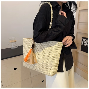 Detailed shot of beige woven straw tote bag with vibrant orange and brown fringe charms