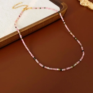 Détail d'un collier de perles roses et blanches avec un fermoir doré sur support en bois