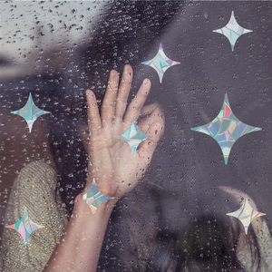 Rainbow prism star window clings with holographic effect on rainy glass surface