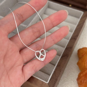 Macro detail of silver pretzel heart pendant on a fine snake chain necklace