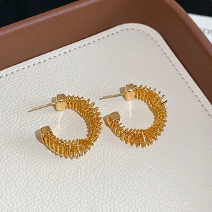 Macro detail of gold-plated C-shaped earrings with twisted wire texture on leather background