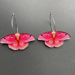 Detail of pink acrylic butterfly earrings with golden patterns and silver metal hoops