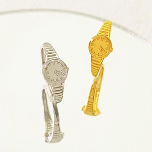 Detailed top view of gold and silver watch-shaped rings reflecting on a mirror surface