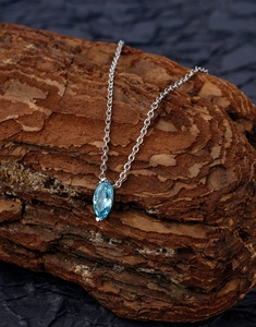 Detailed view of marquise-cut blue zircon pendant on silver chain over natural bark background