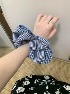 Detail of a blue and white gingham oversized bow scrunchie worn on a female wrist