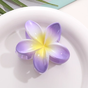 Detail view of a purple and yellow frangipani hair claw clip on a white plate