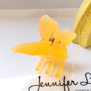 Detailed view of yellow butterfly hair claw clip with golden spring on white board