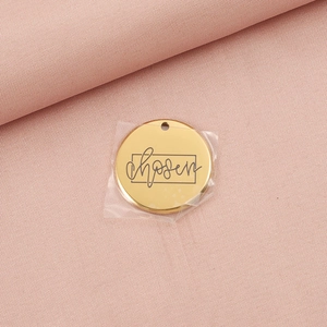 Polished gold round stainless steel pendant with engraved chosen text on pink fabric