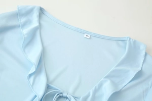 Detail of light blue V-neck top showing ruffle trim, neck ties, and silky fabric texture