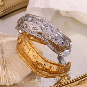 Macro detail of wide open cuff bracelets with molten lava texture in gold and silver finish