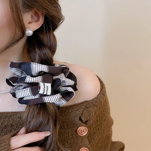 Detail view of brown striped fabric scrunchie with fortune label on braided hair