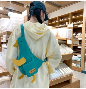 Detail of dark teal duck-shaped canvas crossbody bag with yellow 3D wings and adjustable strap