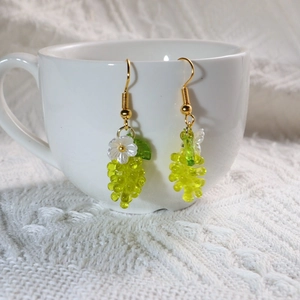 Detail of green grape pendant earrings with small white flowers on a white ceramic cup