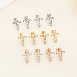 Close-up of cross-shaped earrings in silver, gold and rose gold with white zircon