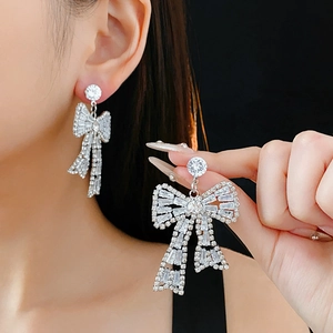 Detail of silver bow earrings with clear zircons worn and held by a model on black background