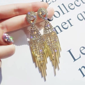 Détails macro des boucles d'oreilles à pompons dorés avec des accents d'émeraude et strass