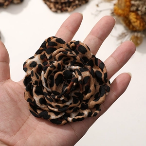 Makroaufnahme einer Kamelienblüte aus Leopardenstoff in der Hand zur Größendarstellung