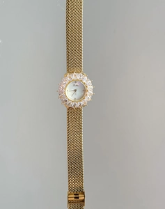 Dettaglio orologio dorato di lusso con ghiera diamantata e cinturino in maglia