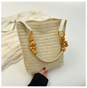 Detail of beige straw tote bag featuring decorative wooden bead handle on white dress