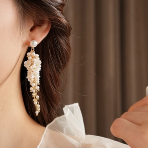 Close-up of elegant gold tassel earrings with white resin flowers and pearls on model