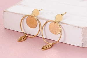 Detail of gold titanium steel earrings with round discs and hollow leaf pendants