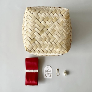 Flat lay of square bamboo gift box with red ribbon, thank you tag, and pearl charm