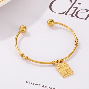Detail of a gold stainless steel open bangle with beads and a symbolic rectangular charm