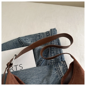 Detail of dark brown suede shoulder bag with leather strap on denim background