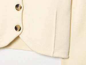 Detailed close-up of cream knit cardigan hem featuring tortoise shell buttons texture