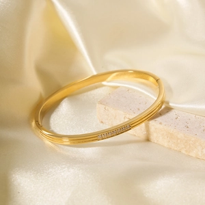 Luxurious 18k gold stainless steel bangle with sparkling zircons on cream silk background