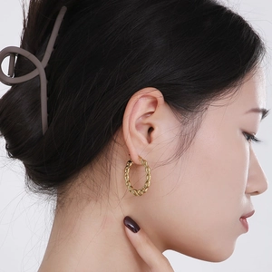 Détail de boucles d'oreilles créoles torsadées dorées portées par un mannequin