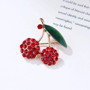 Detailed close-up of a gold cherry brooch with red rhinestones and green enamel leaves
