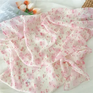 Detail of pink chiffon scarf with cherry and bow print featuring a soft fabric label