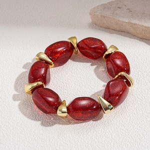 Macro detail of red glitter resin beads and gold geometric spacers on an elastic bracelet