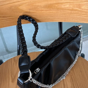 Close-up of a black pleated shoulder bag featuring a woven handle and silver metal chain