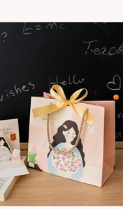 Detail of pink teacher gift bag with golden handle, ribbon bow and 3D card on desk