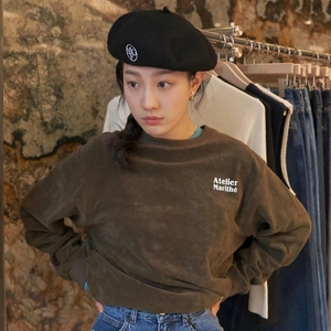 Detail of a brown velvet sweatshirt with white logo embroidery and a black beret hat