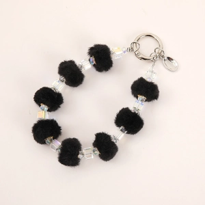 Plush ball and transparent beaded bag charm with metal clasp on beige background